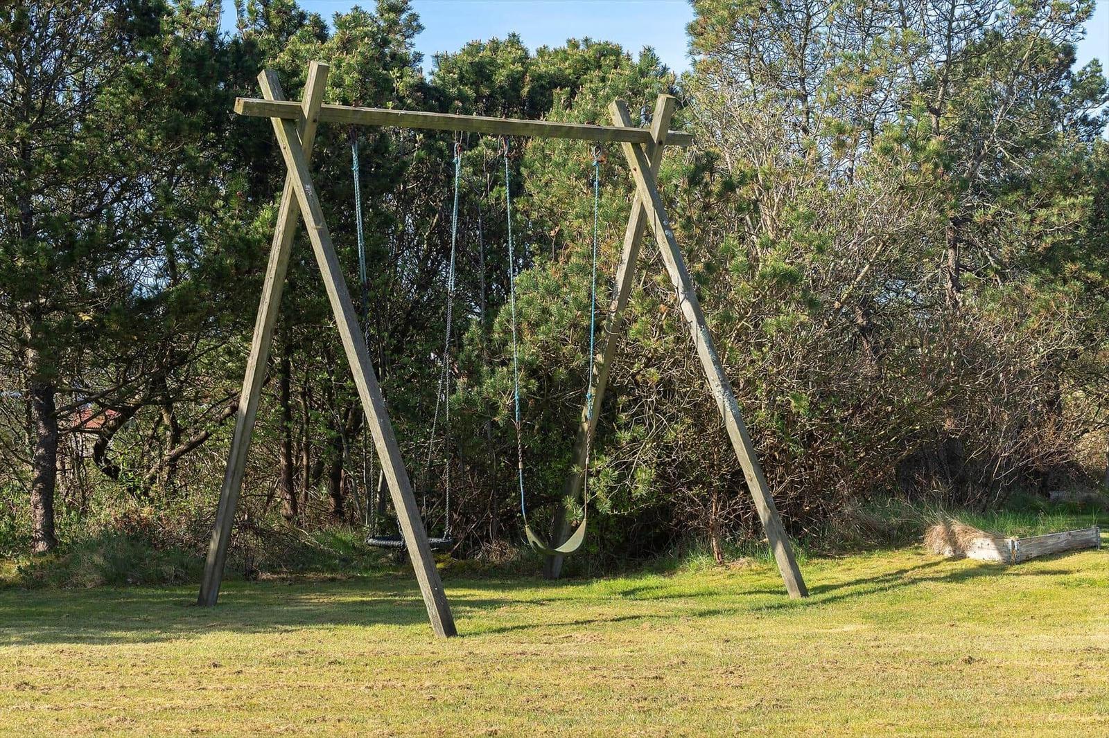 Holzschaukel mit zwei Sitzgarnituren auf grünem Rasen vor Bäumen.