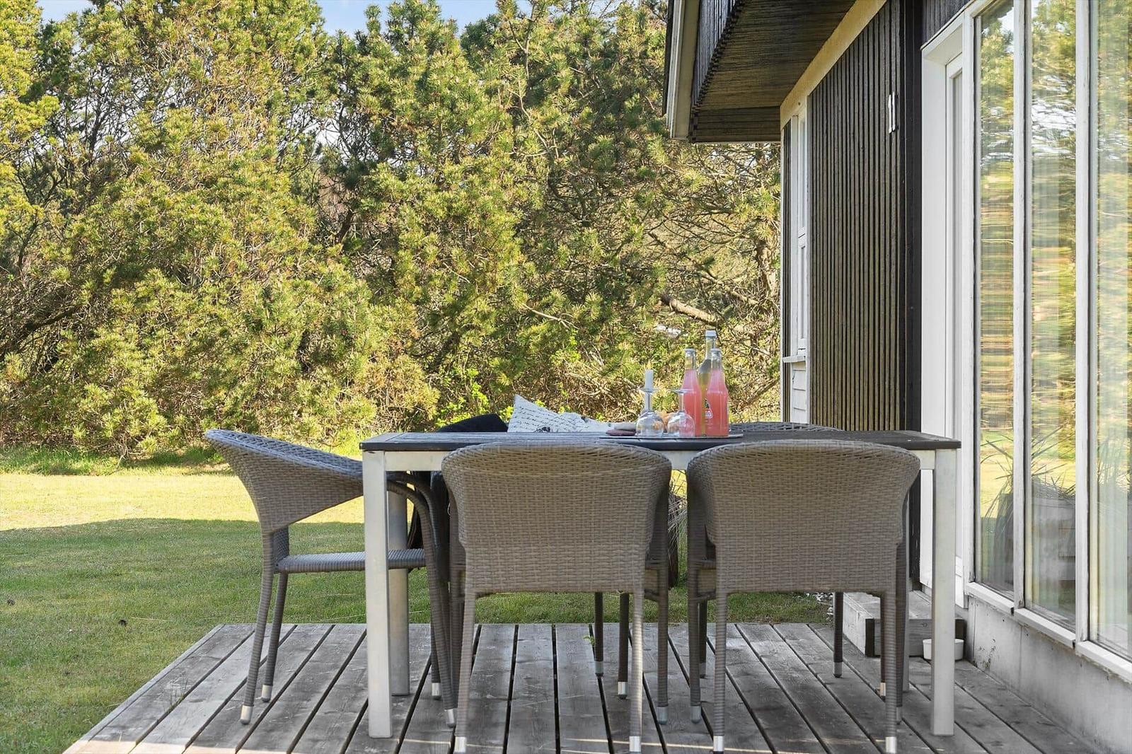 Terrasse mit Tisch und Stühlen, Blick auf grüne Bäume und Hauswand.