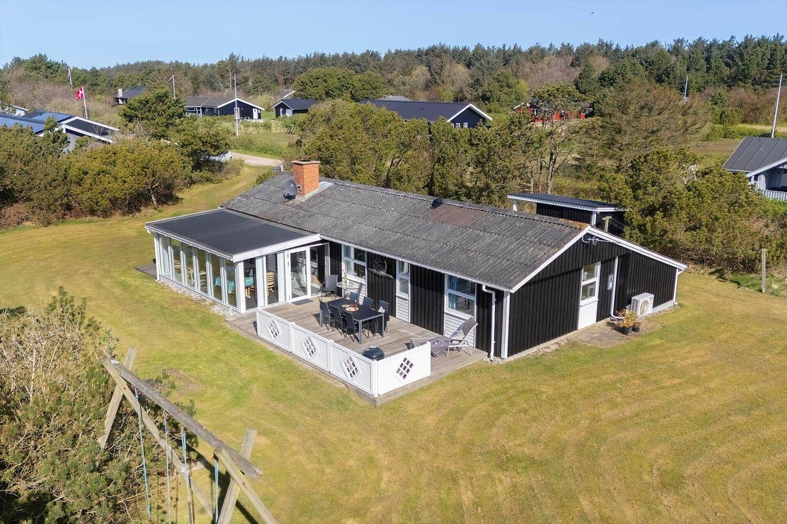 Schwarzes Haus mit Terrasse und Garten. Umgeben von Bäumen und Grasflächen.