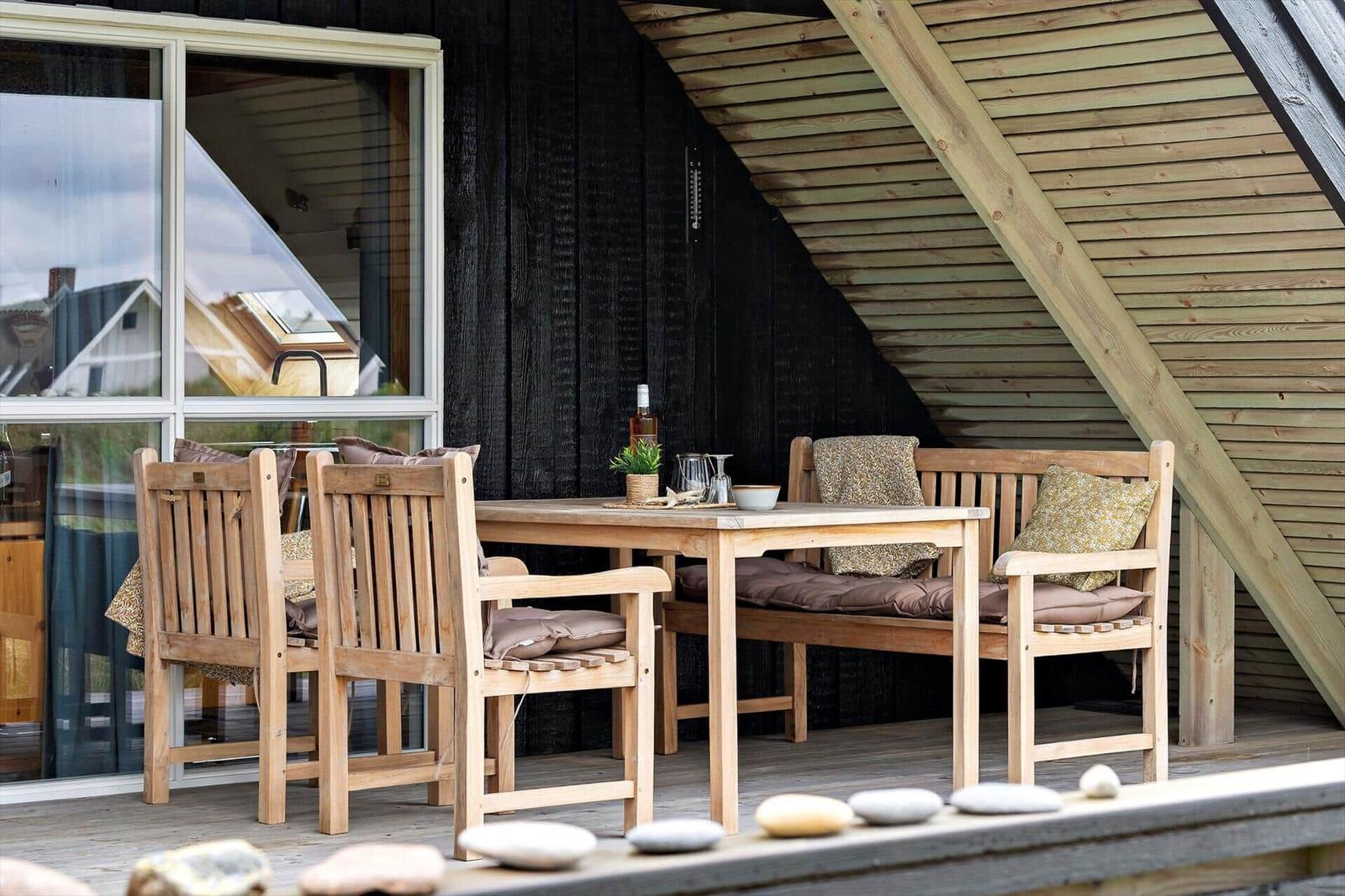 Holztisch mit Stühlen und Bank auf Terrasse unter Holzschindel-Dach.