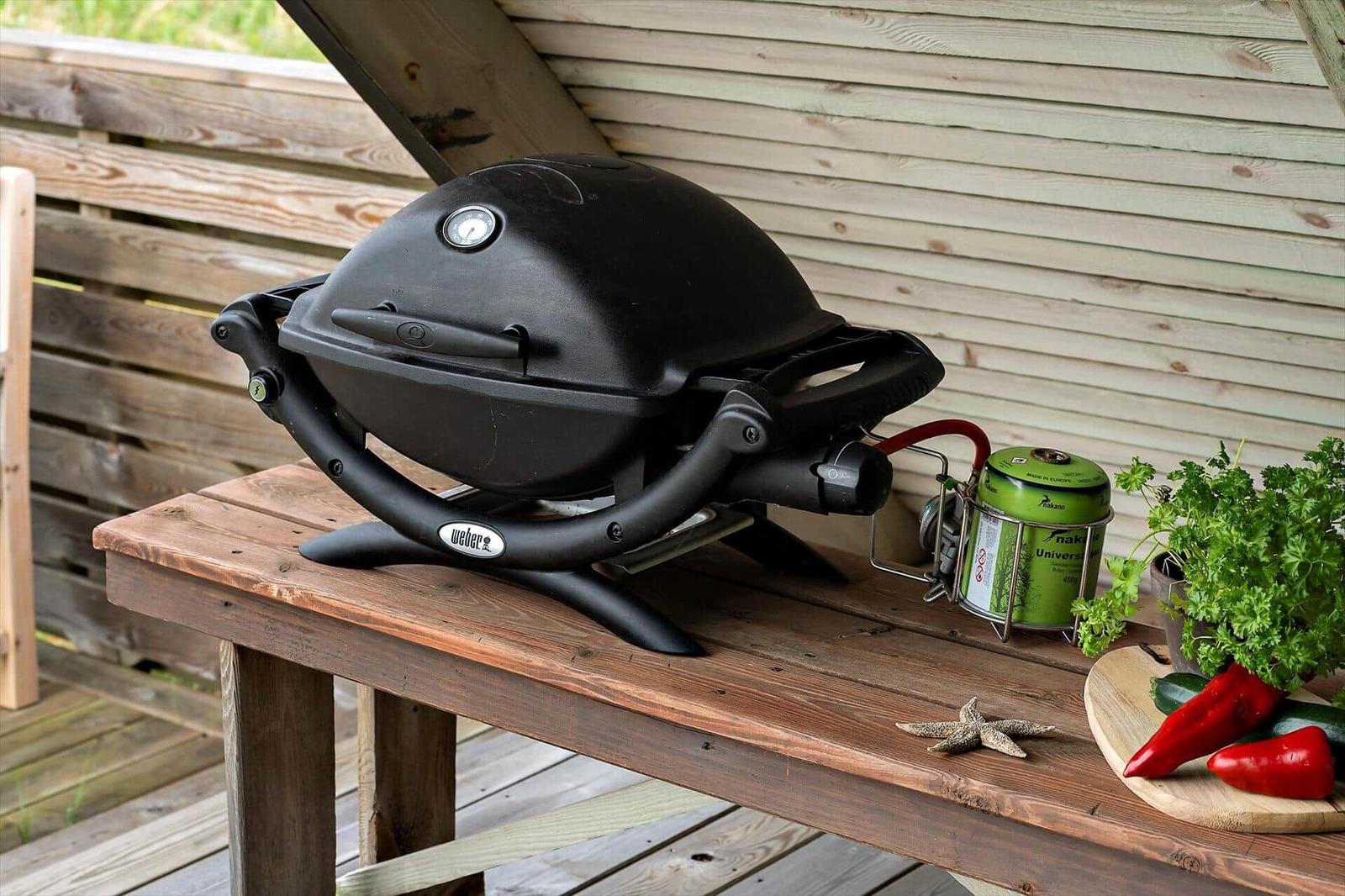 Schwarzer Grill auf Holztisch mit Brenner, Pflanzen und roten Chilis.