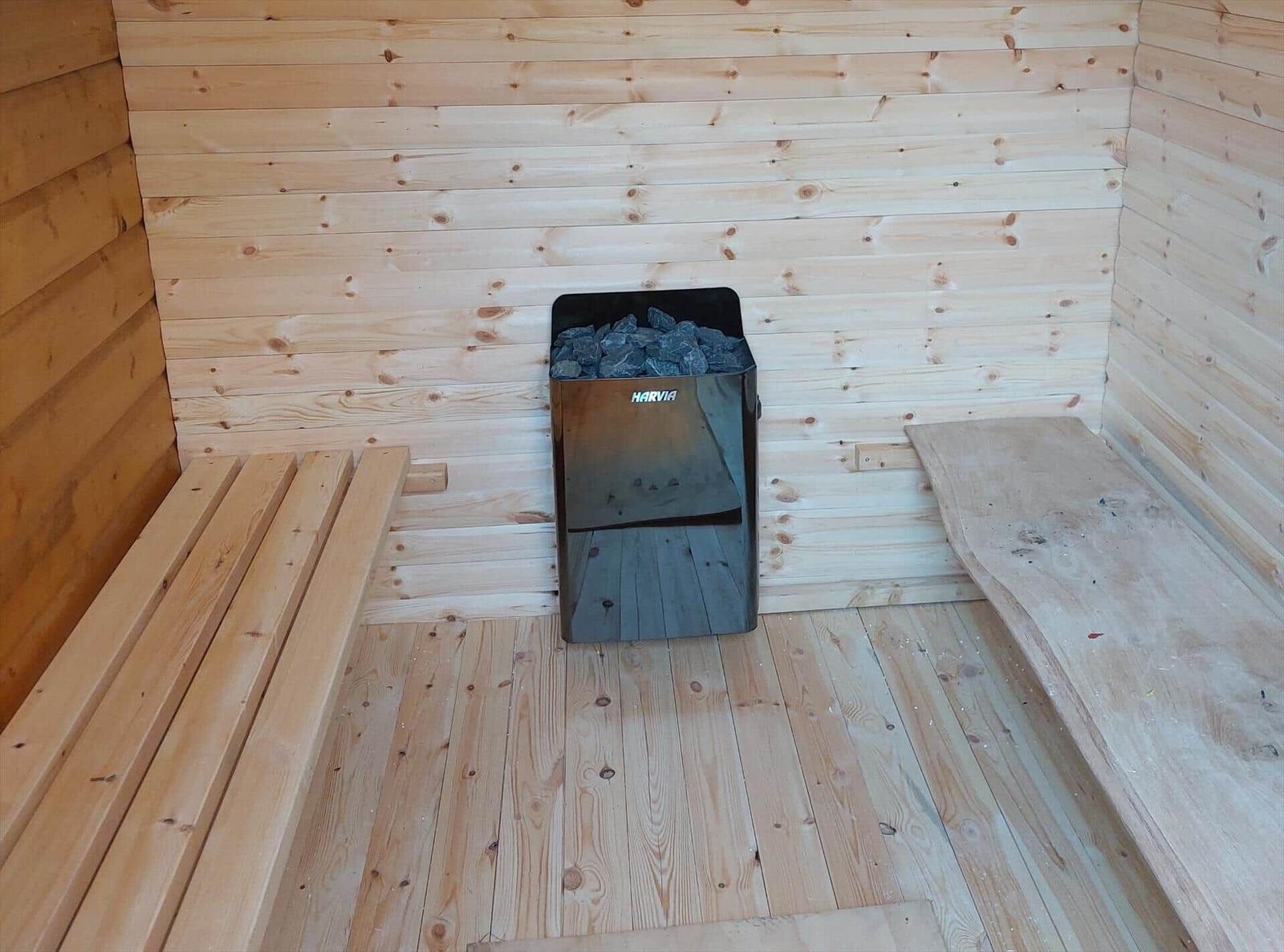Sauna with wooden walls, bench, and Harvia stove with stones.