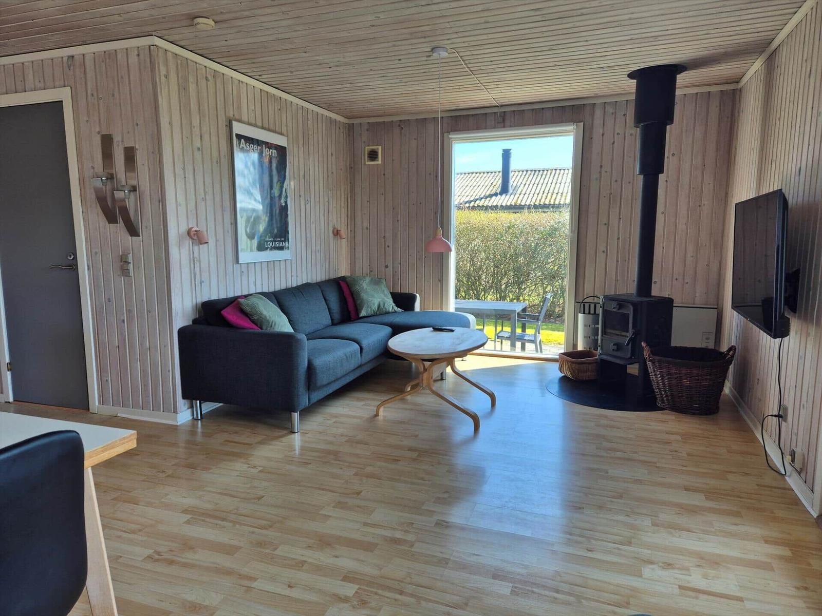 Wohnzimmer mit Sofa, Kamin und TV. Holzdielen und Wandverkleidung.