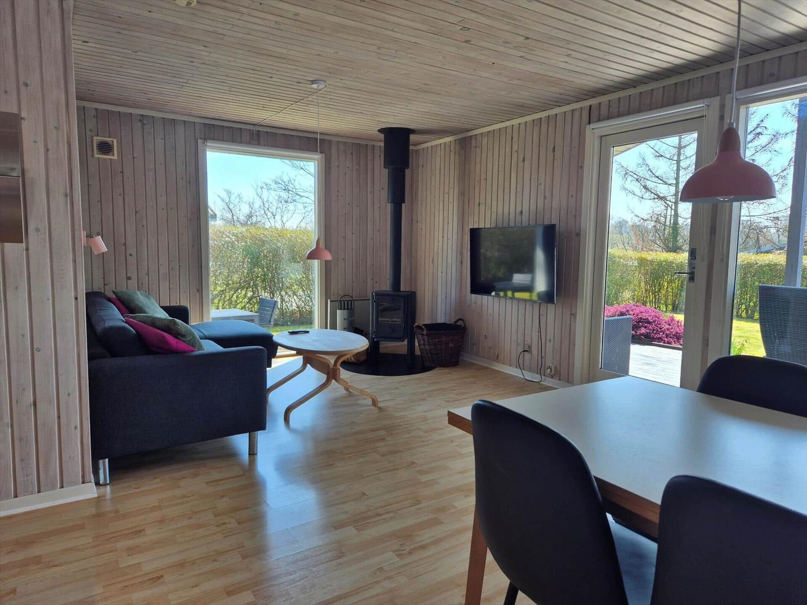 Wohn- und Essbereich mit Holzwand, Kaminofen, TV und Terrassentür.