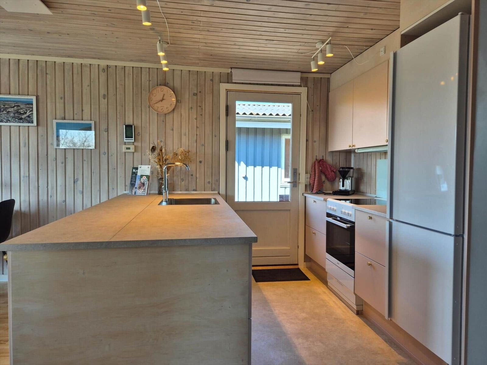 Küche mit Holzwand, Insel, Kühlschrank und Ofen. Tür führt nach draußen.