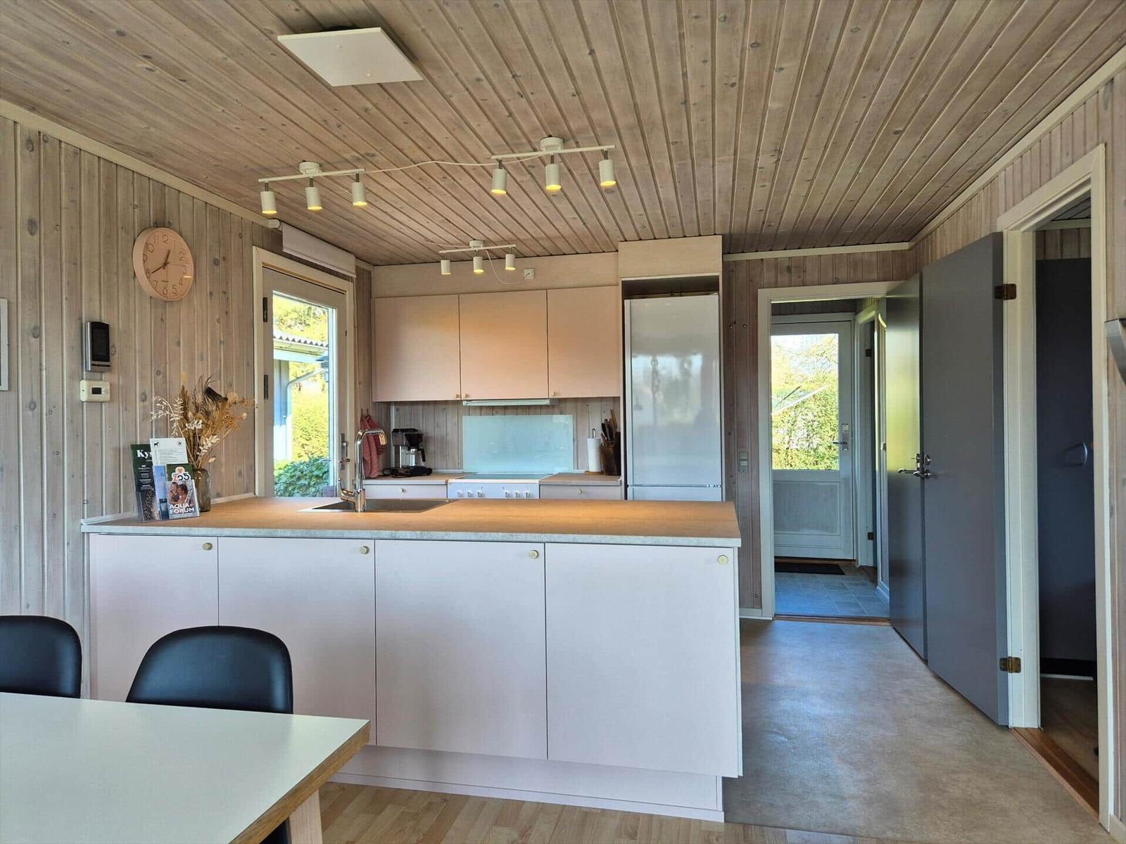 Küche mit Holzwand und -decke, Arbeitsplatte, Kühlschrank und Türen zu anderen Räumen.