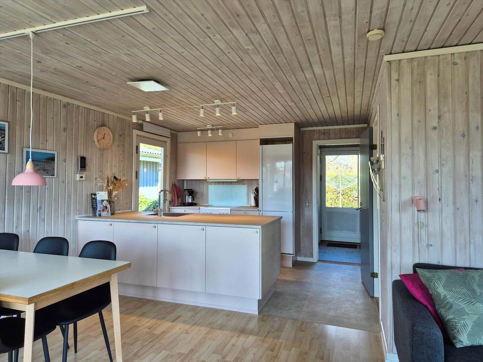 Küche mit Essbereich und Wohnbereich. Holzwände und -decke. Tür zum Garten.