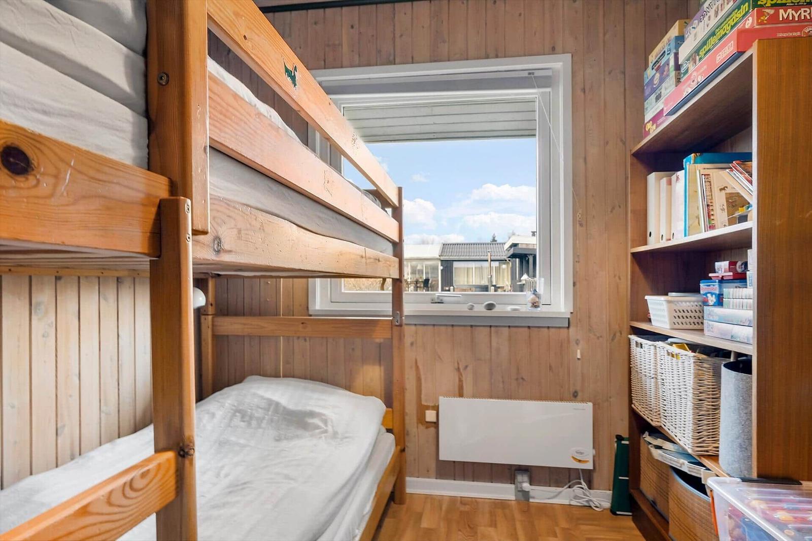 Room with bunk bed, bookshelf, and window view of outdoor area.