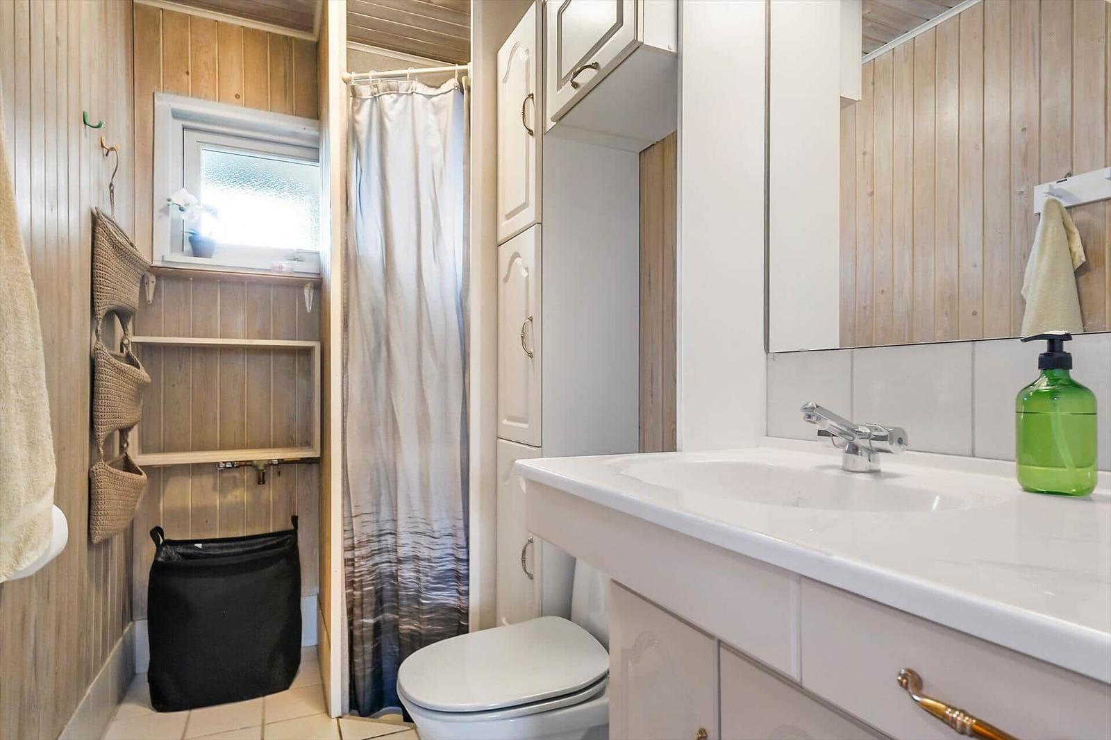 Bathroom with sink, mirror, shower, and toilet. Wooden walls and white fixtures.