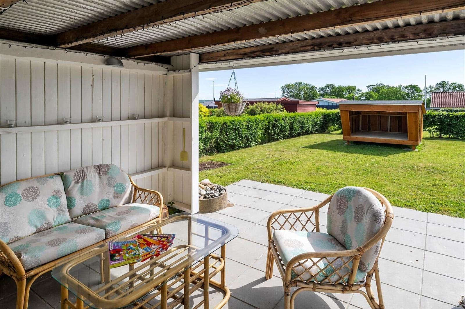 Terrace with seating group, glass table, and view of garden with wooden shed.