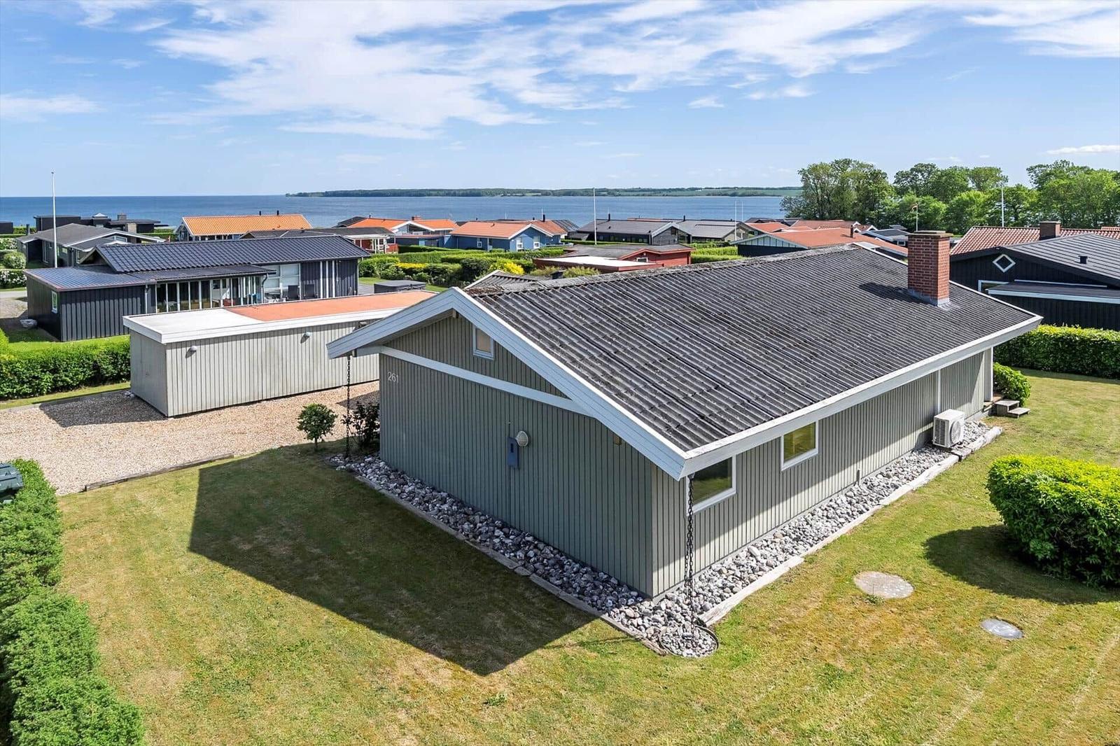A gray house with roof and garden, view of water and houses