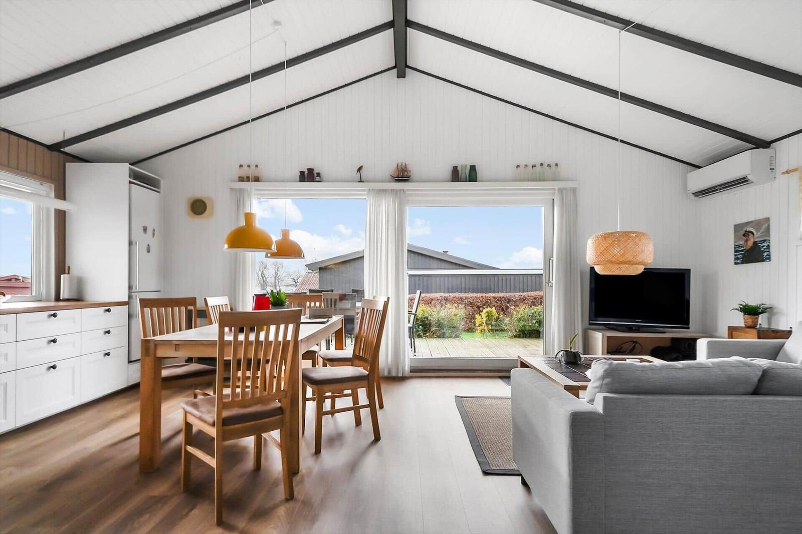 Living area with dining space, sofa, and TV. Large windows overlooking the terrace.