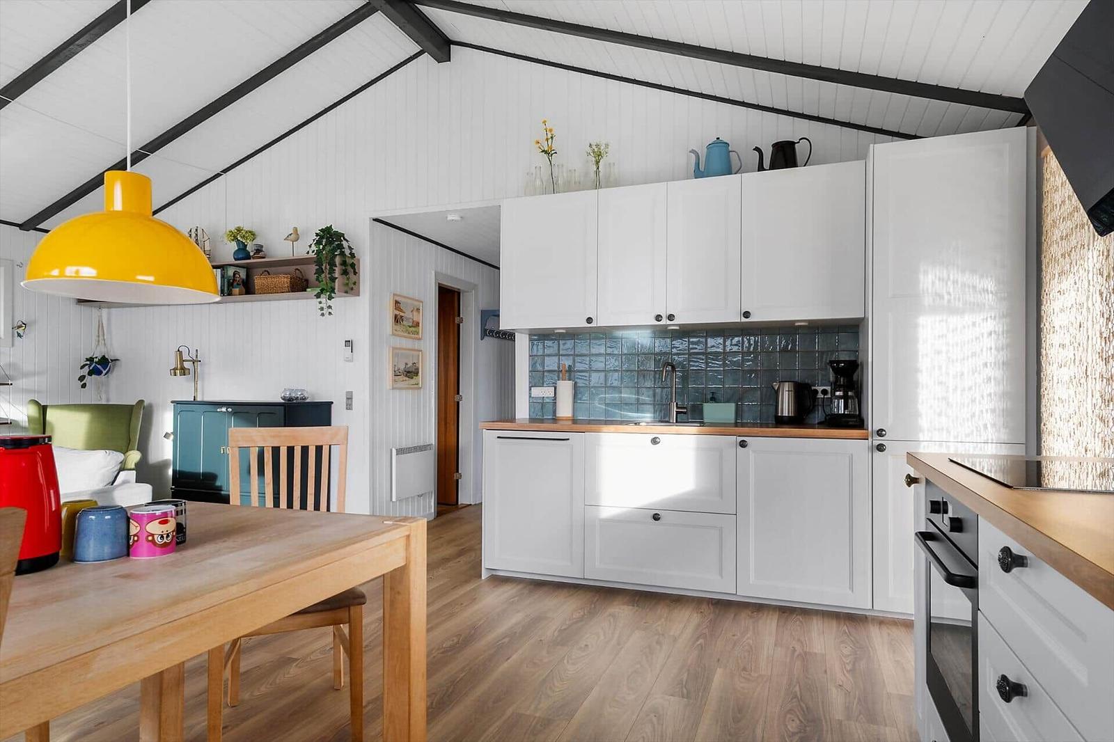 Kitchen with white cabinets, wooden countertops, and blue tiles. Dining area with table and chairs.