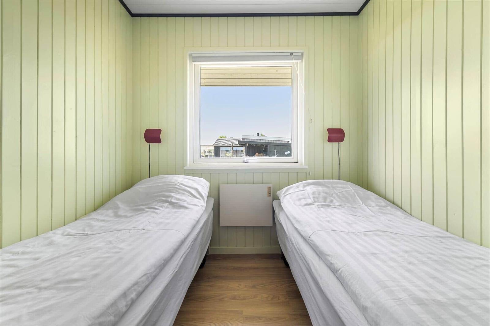 Two beds with white sheets are in a room with green paneled walls and a window.