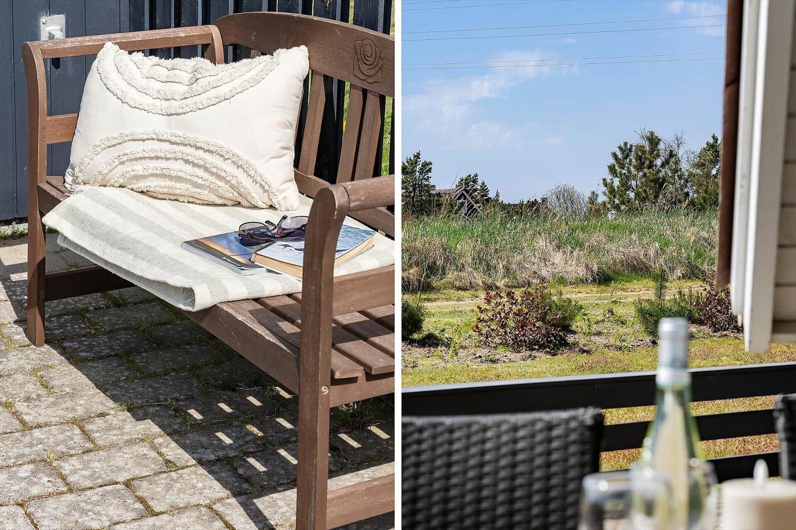 Holzbank mit Kissen und Buch auf Terrasse. Blick auf Grünfläche und Himmel.
