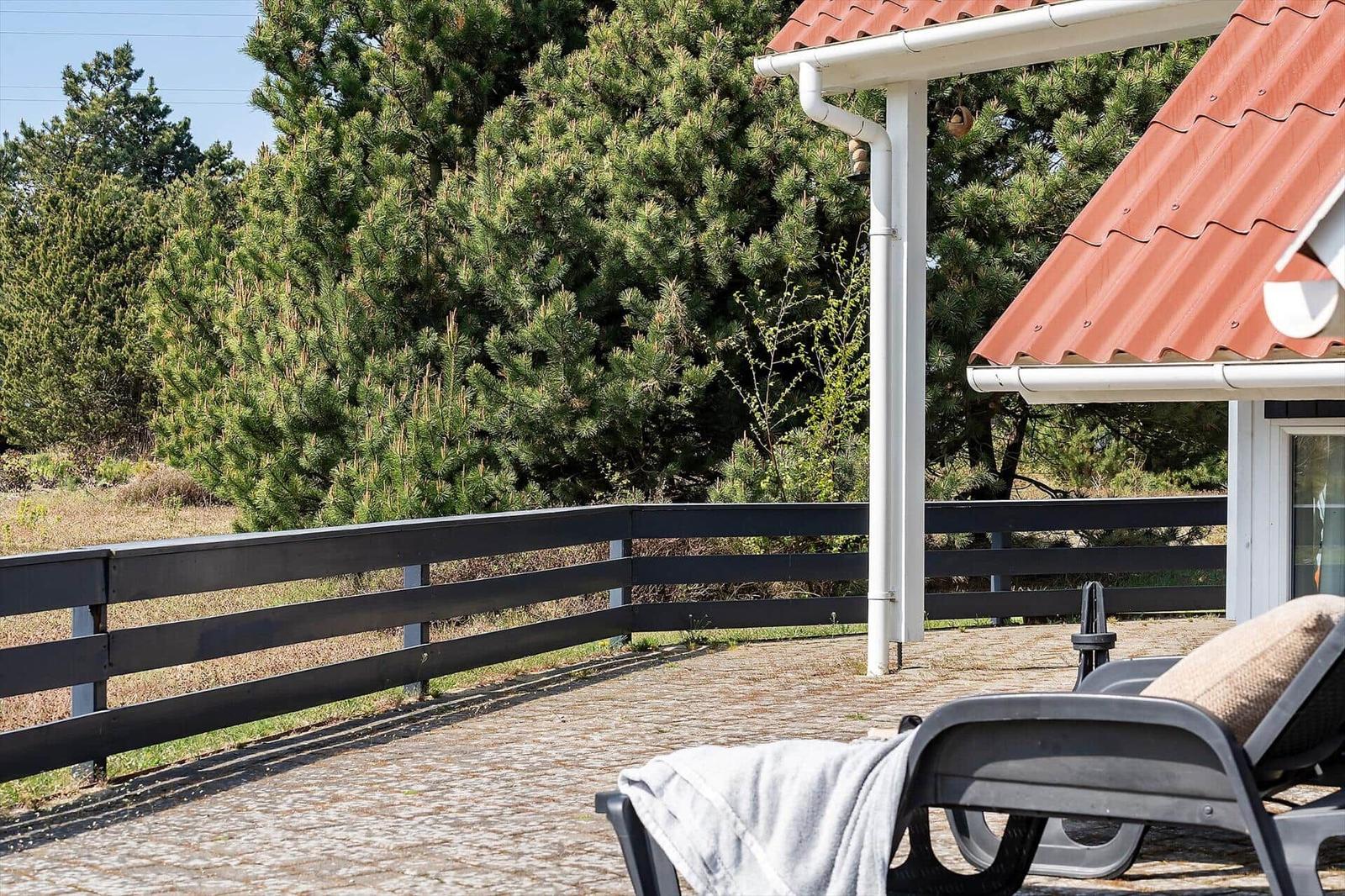 Terrasse mit Liegestuhl, rotem Dach und Holzgeländer vor grünen Bäumen.