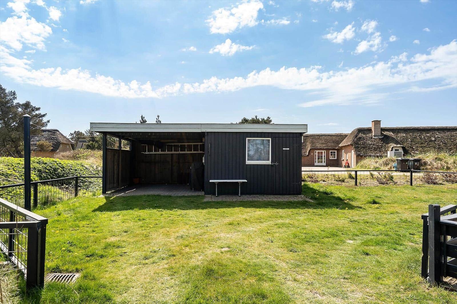 Ein schwarzes Gebäude mit offener Garage und Fenster. Grasfläche und Hütten im Hintergrund.