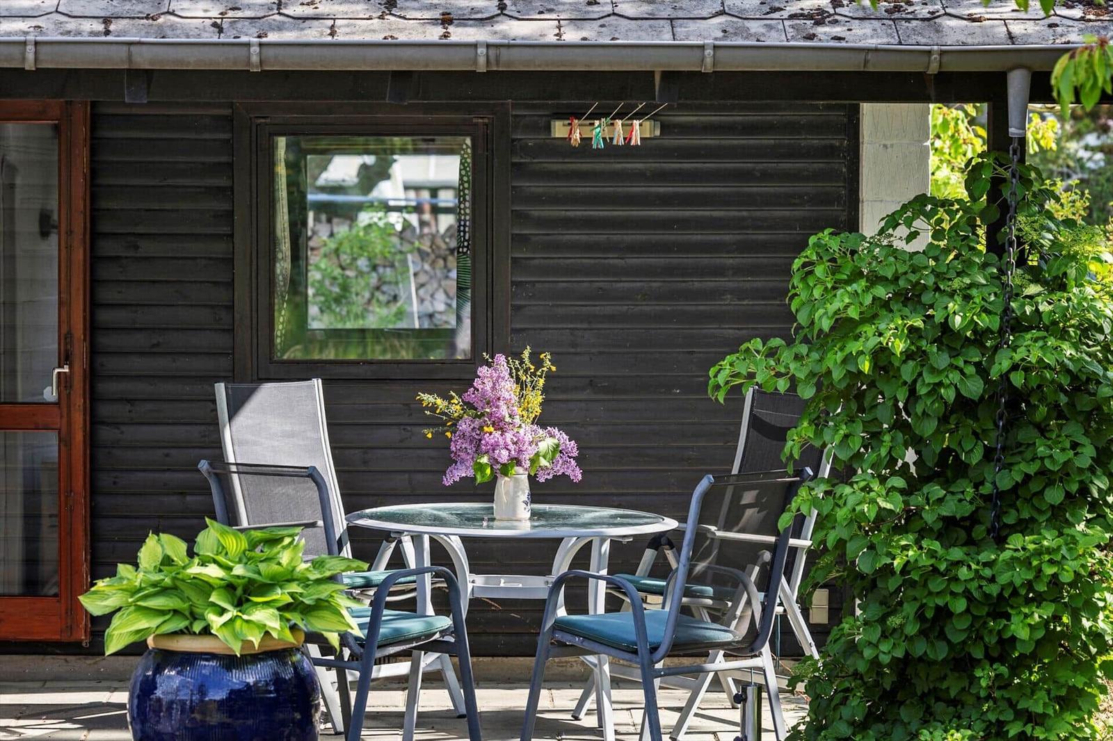 Patio with table, chairs, and flowers in front of a dark wood house.