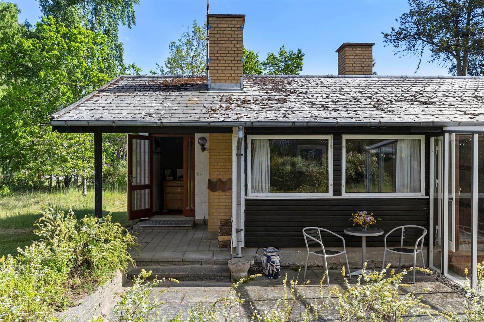 House with terrace, garden, and two chimneys under blue sky.