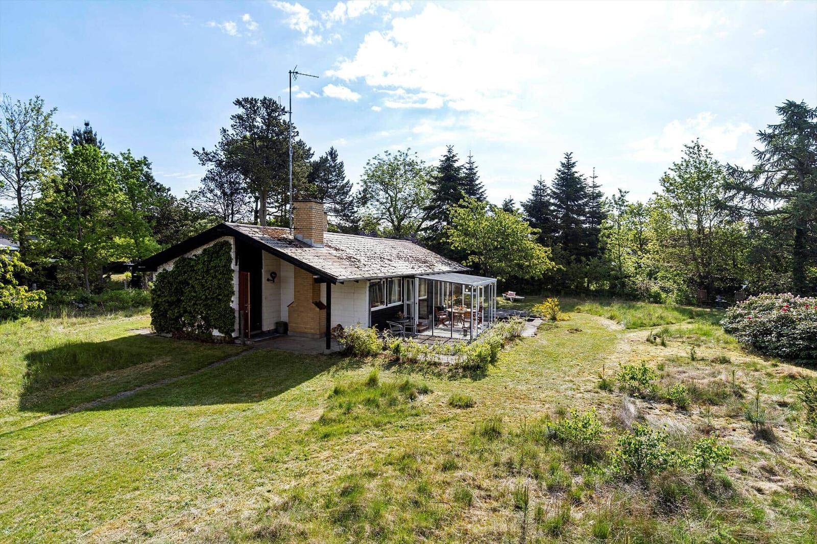 A house with a terrace and garden, surrounded by trees and grass.