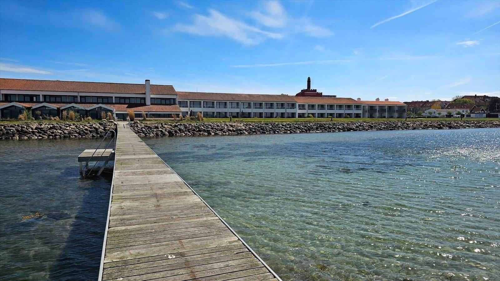 Wooden pier leads to a building by the water with a red roof.