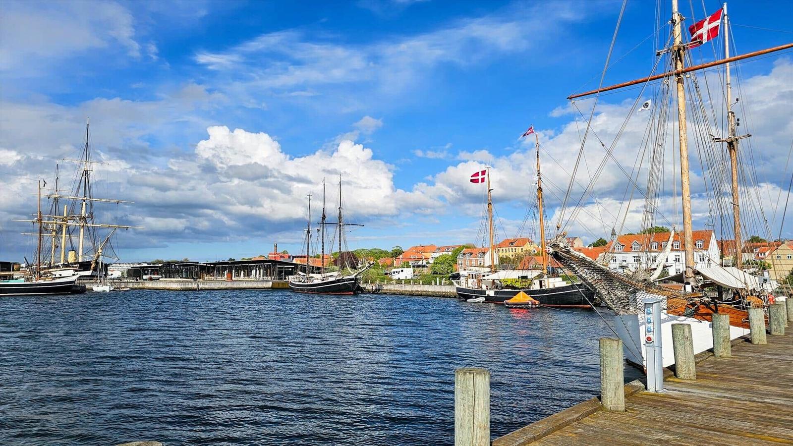 Harbor with sailing ships and red roofs under blue sky.