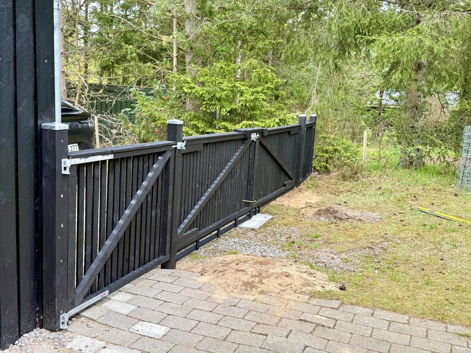 Black wooden gate with driveway and green area in the background.