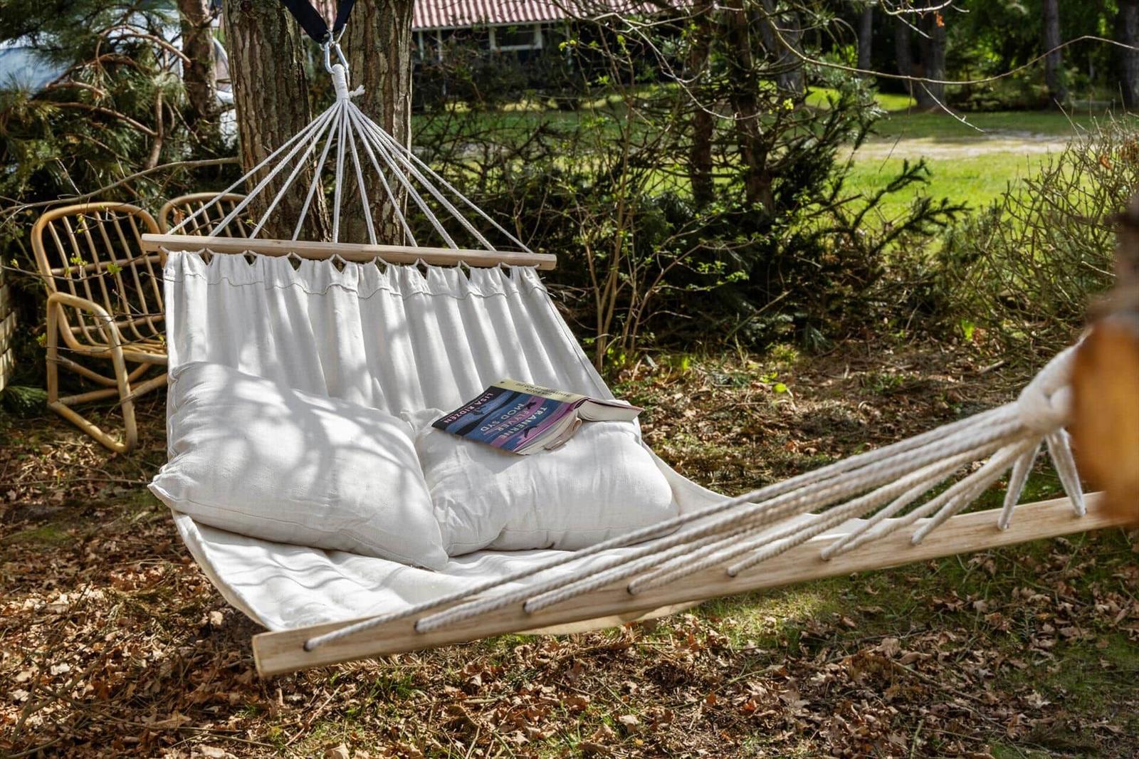 Hammock with cushions and book between trees outdoors