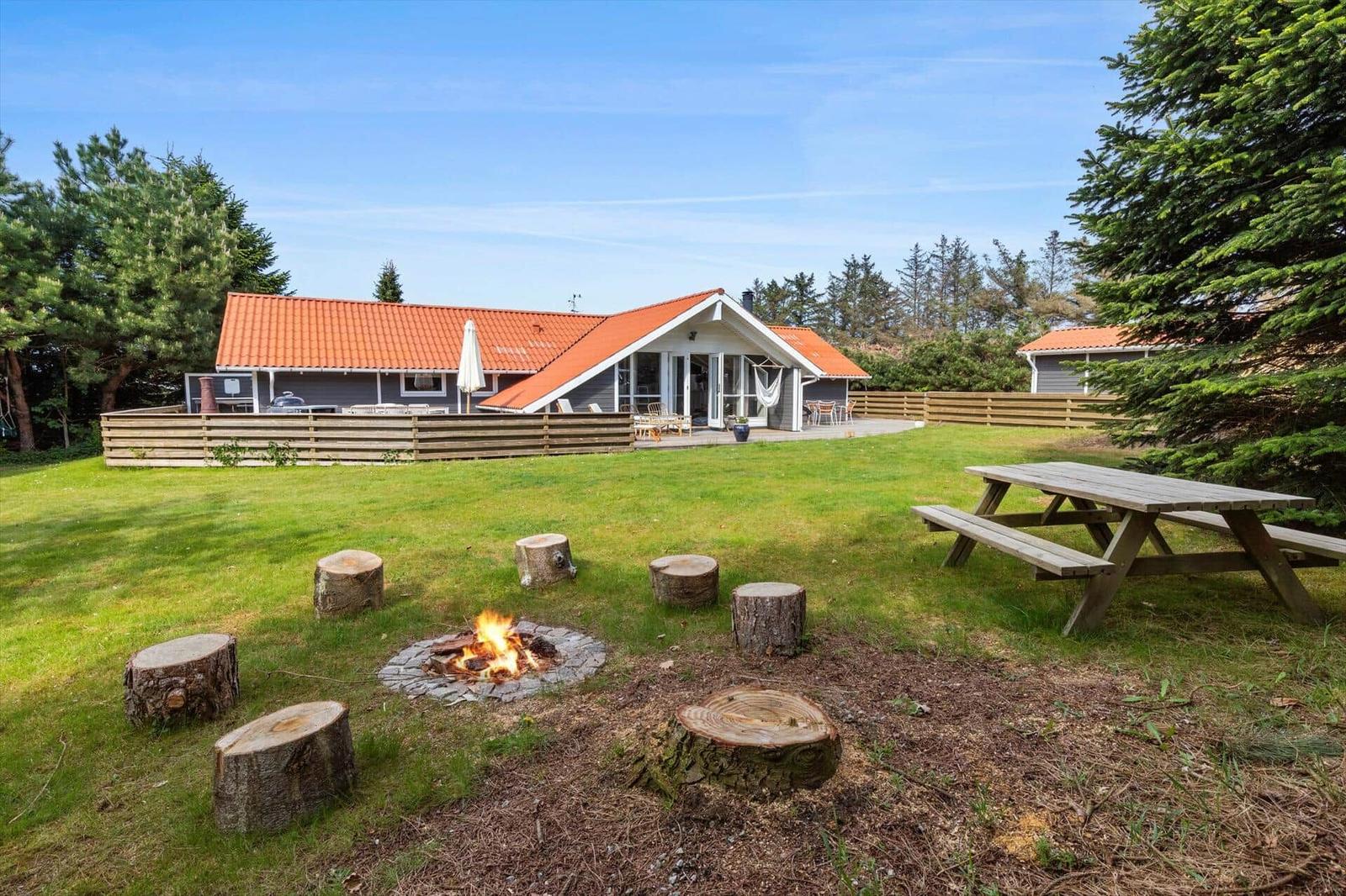 House with garden, fire pit, and picnic table. Red roof ridge and wooden fence.