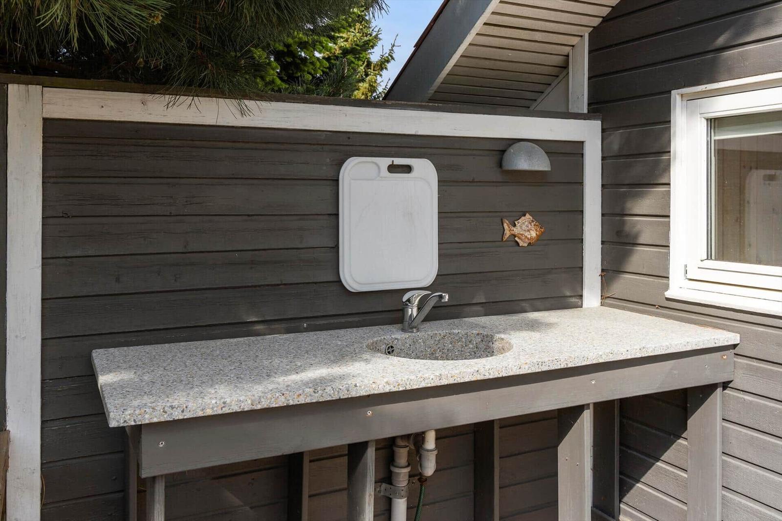 Outdoor sink with countertop, faucet, and cutting board on the wall.