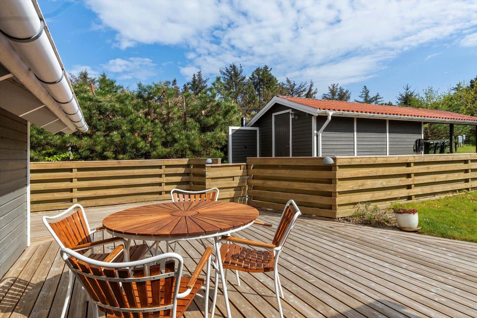 Wooden terrace with table and chairs, surrounded by fence and forest.
