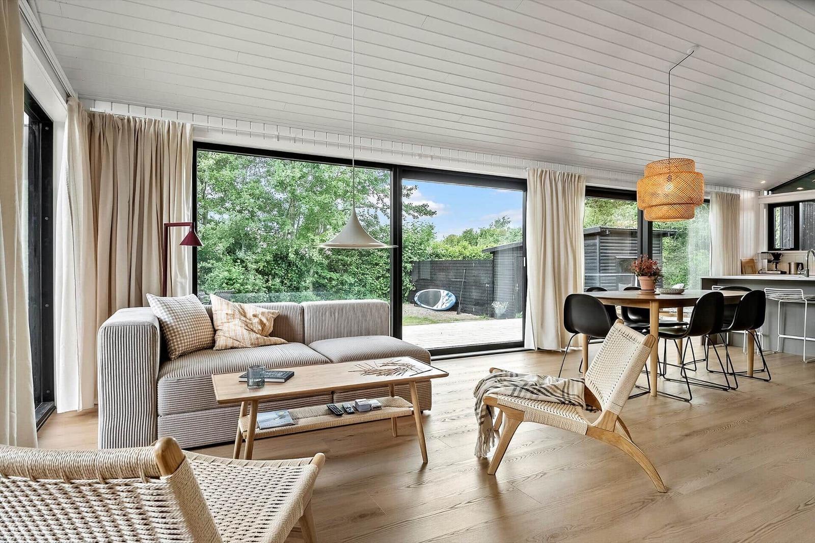 Living and dining area with sofa, table and chairs. Large windows with view of garden.