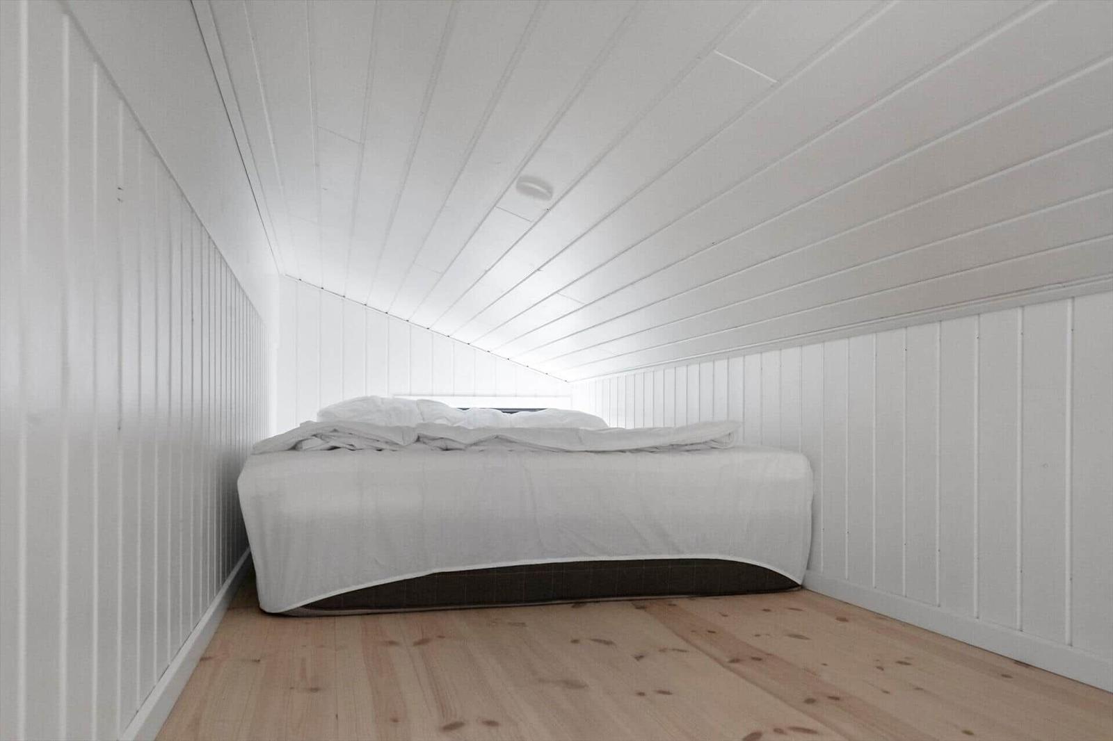 Bedroom with white bed and wooden floor. Walls and ceiling are white clad.