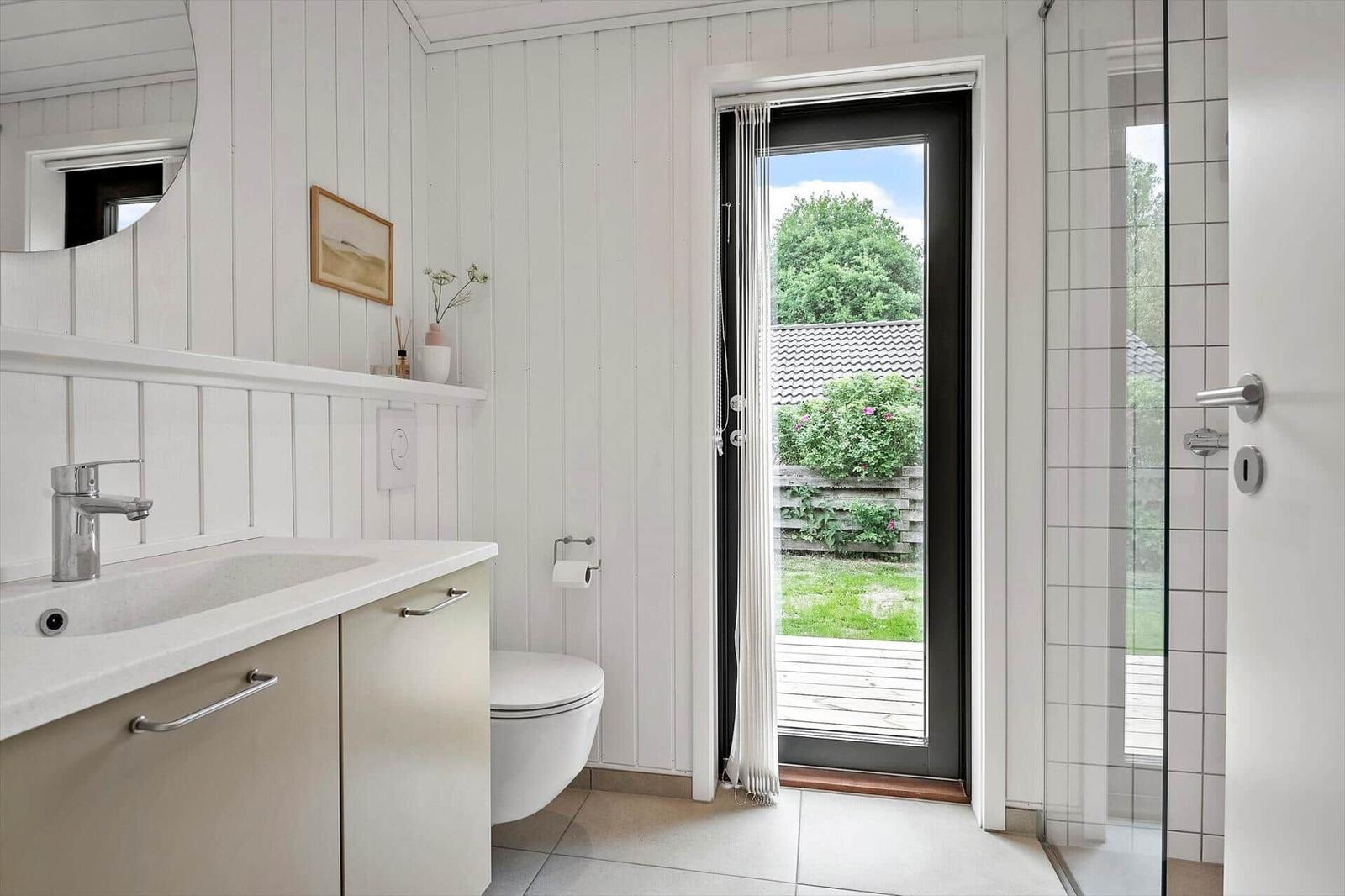 Bathroom with sink, toilet, and shower. Doorway to terrace with garden view.