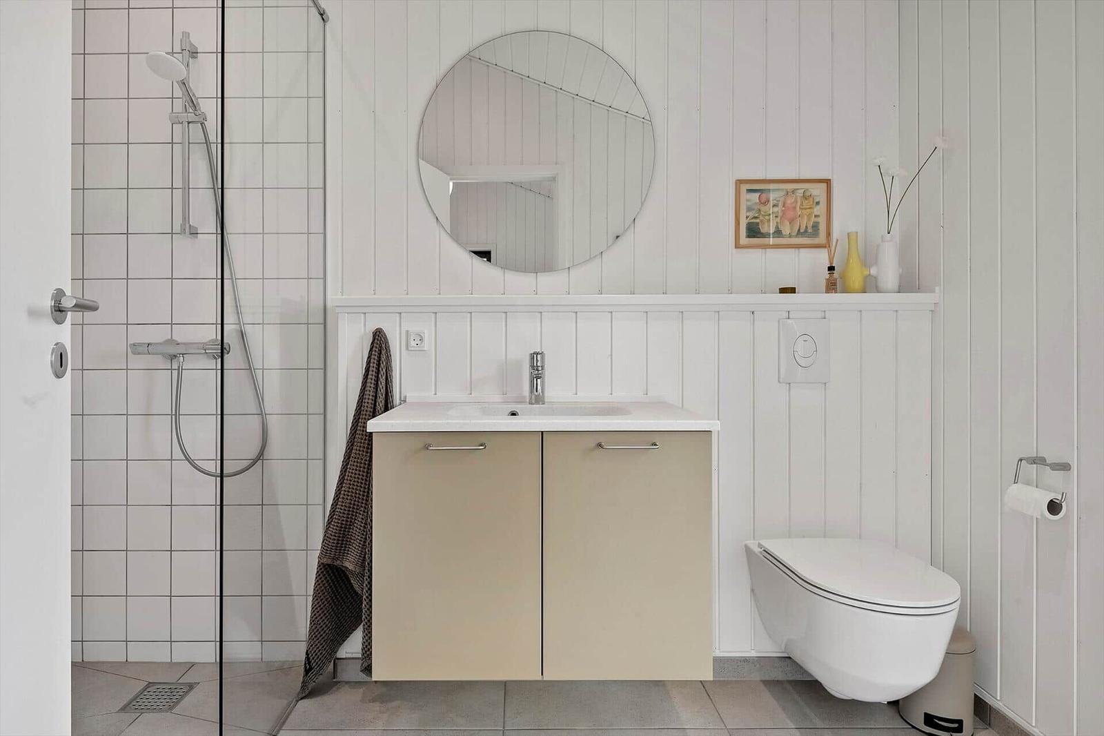 Bathroom with shower, sink and toilet. White paneling on the walls.