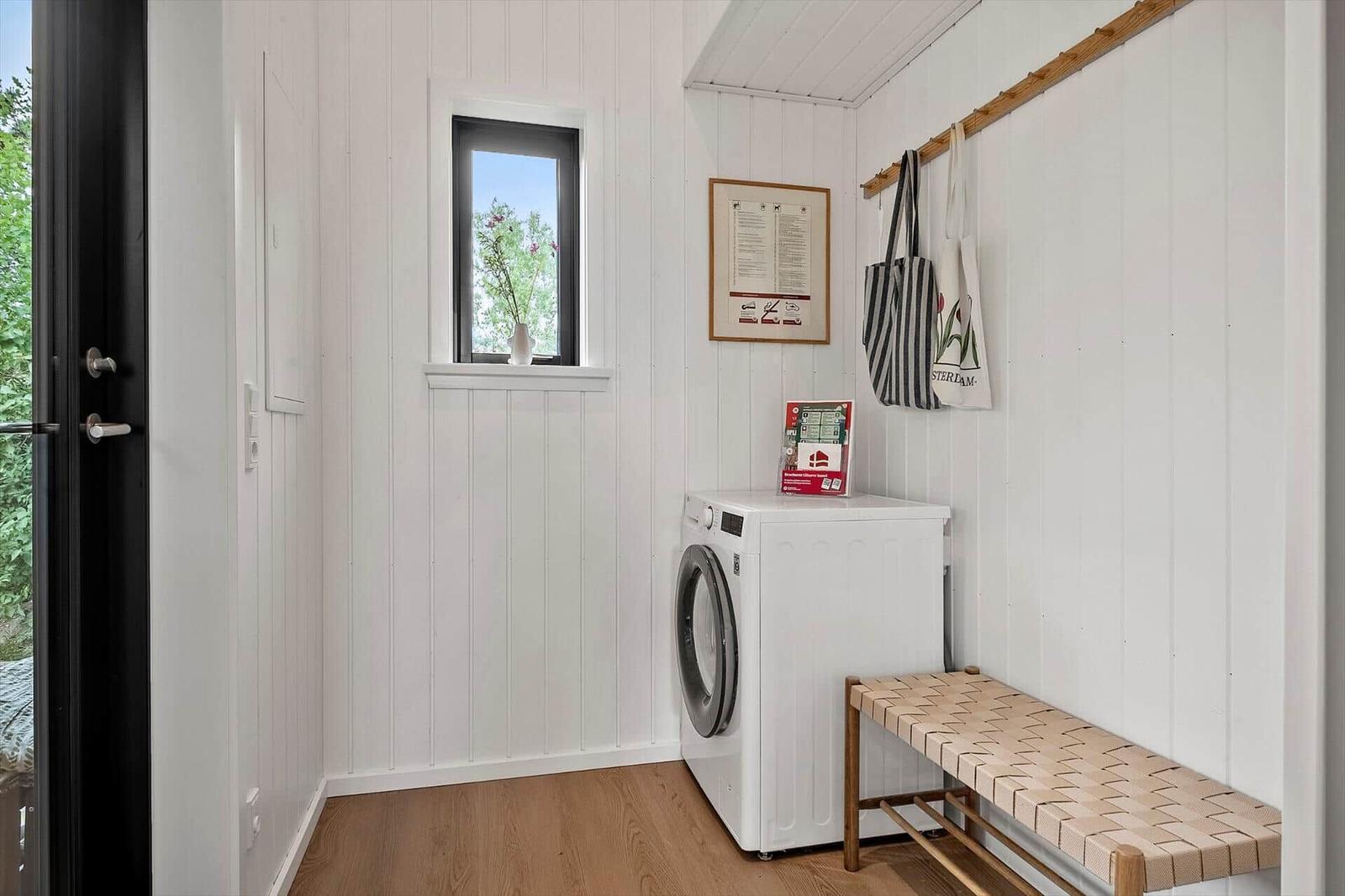 Room with washing machine, bench, and window. Walls with wood paneling and hooks.