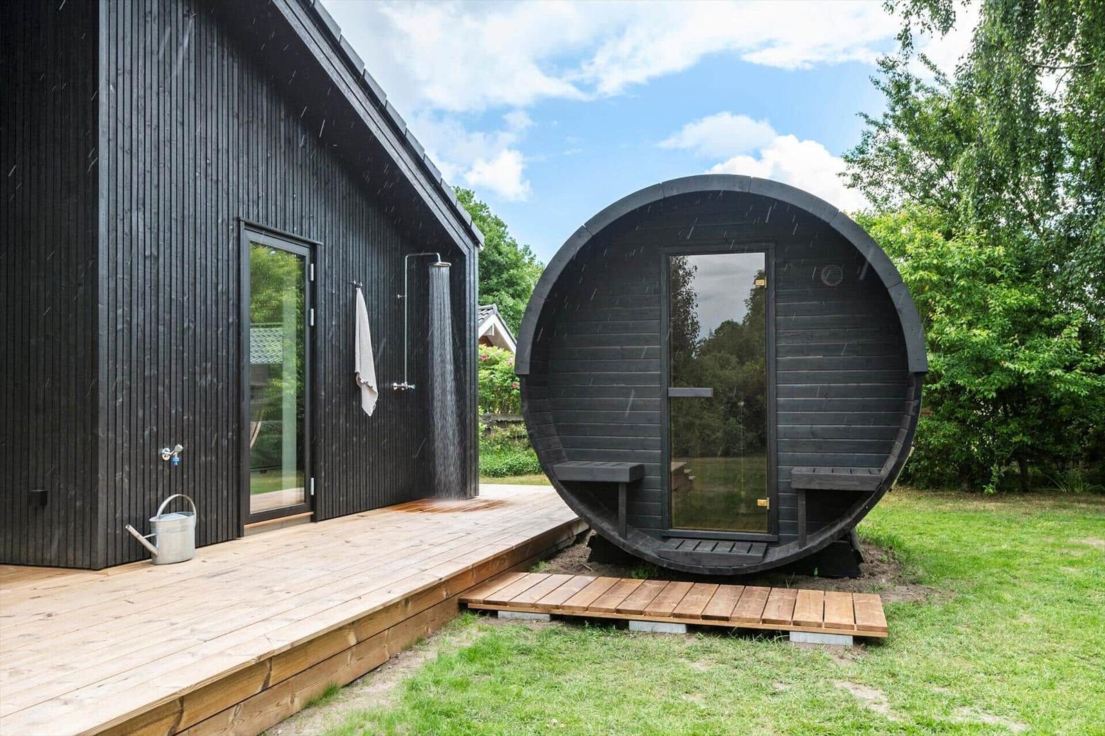 Black wooden cabin with shower and round sauna in the garden