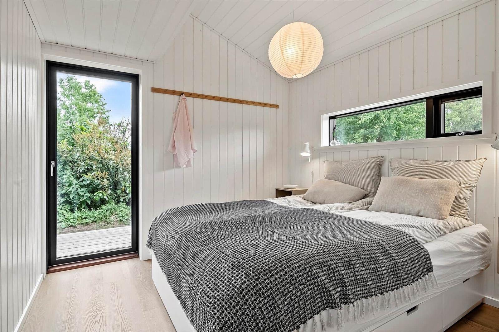 Bedroom with bed, windows, and door to garden. Wooden walls and ceiling.