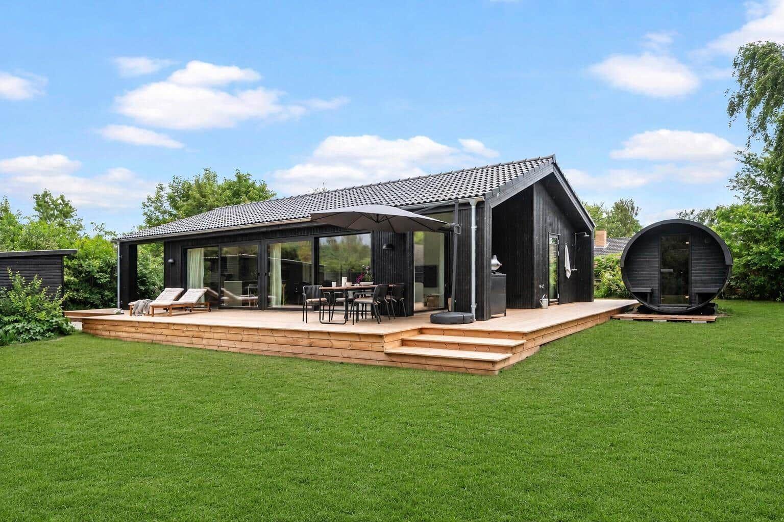Modern villa with wooden terrace, seating, and round sauna in the garden.