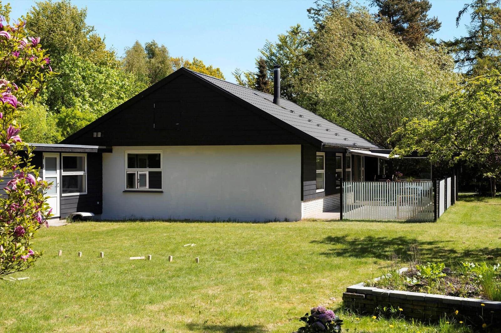 A house with a black roof and white facade. Front yard with grass and flowers.