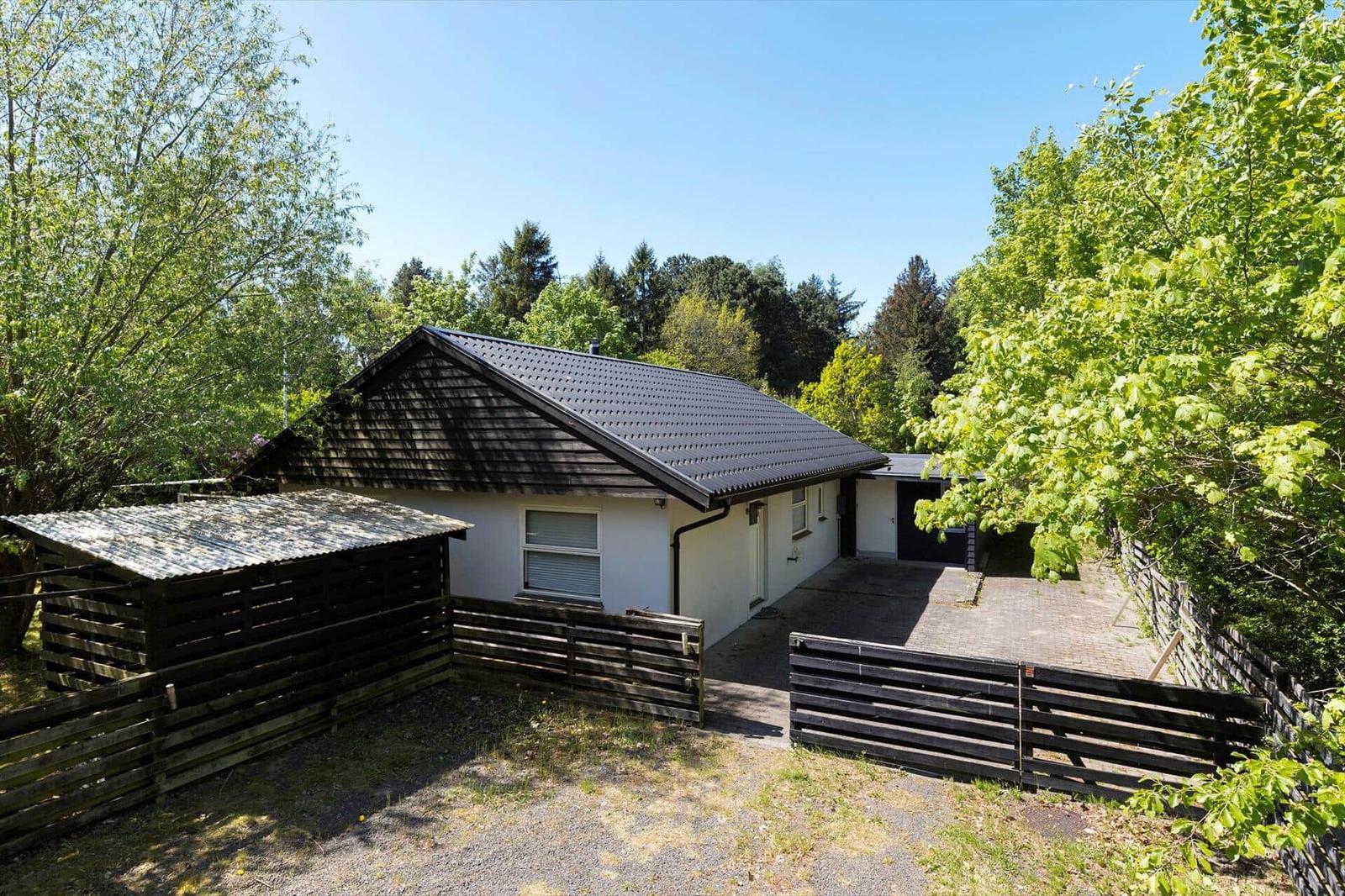 A white house with a black roof and wooden fence in the greenery.