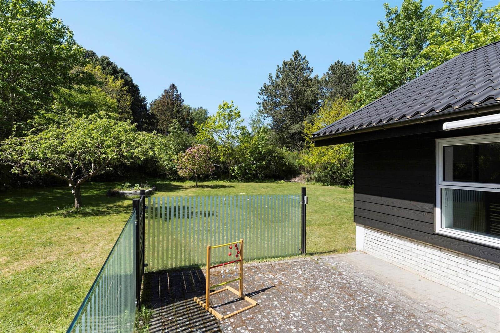 Backyard with play equipment, glass fence, and green lawn. Beside a black-clad house.