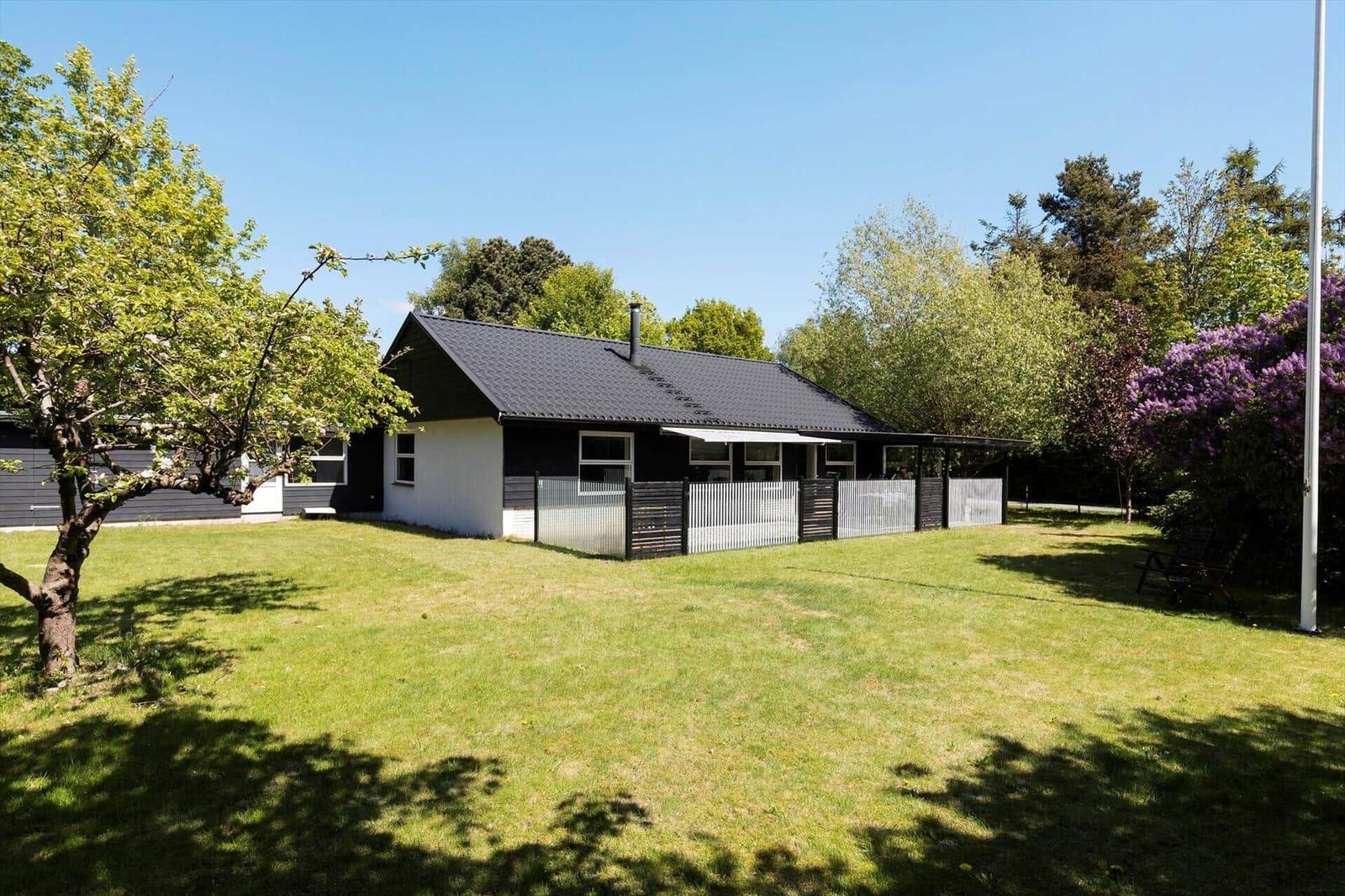 A house with a black roof and white facade, surrounded by grass and trees.