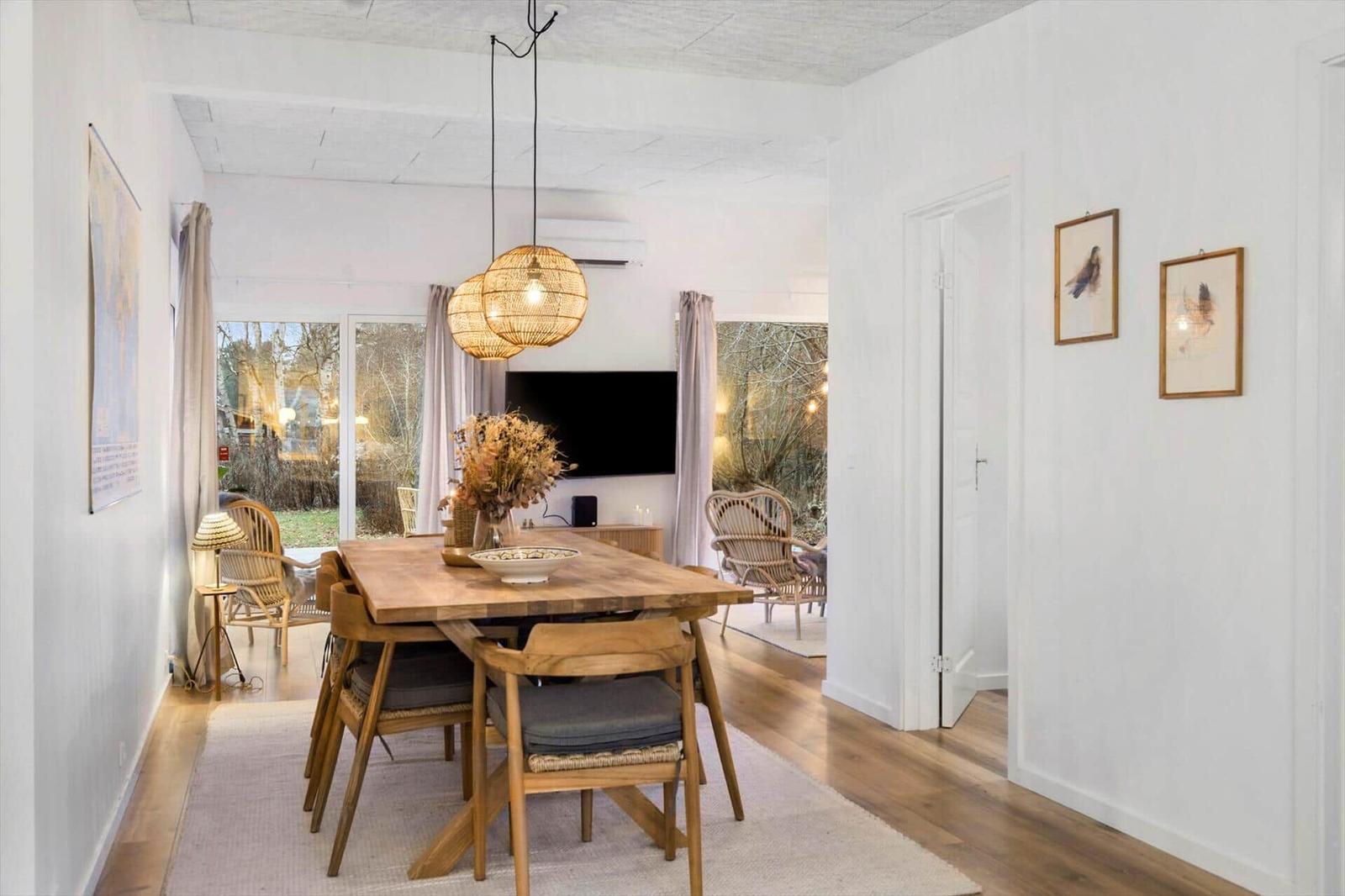 Kitchen with dining area and living room. Wooden floor, white cabinets, dining table with chairs.