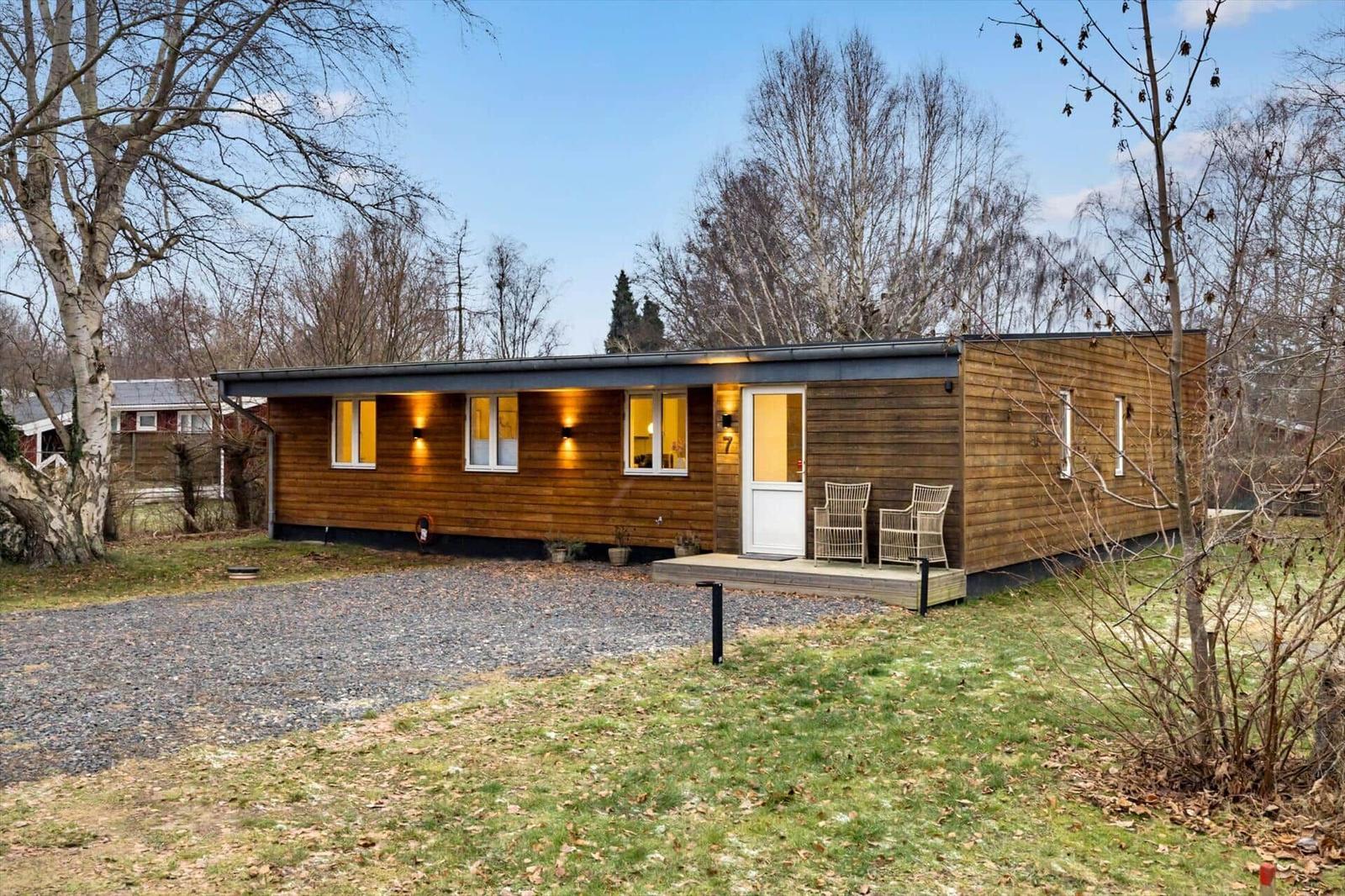 Modern wooden cabin with terrace, garden, and trees in the background.