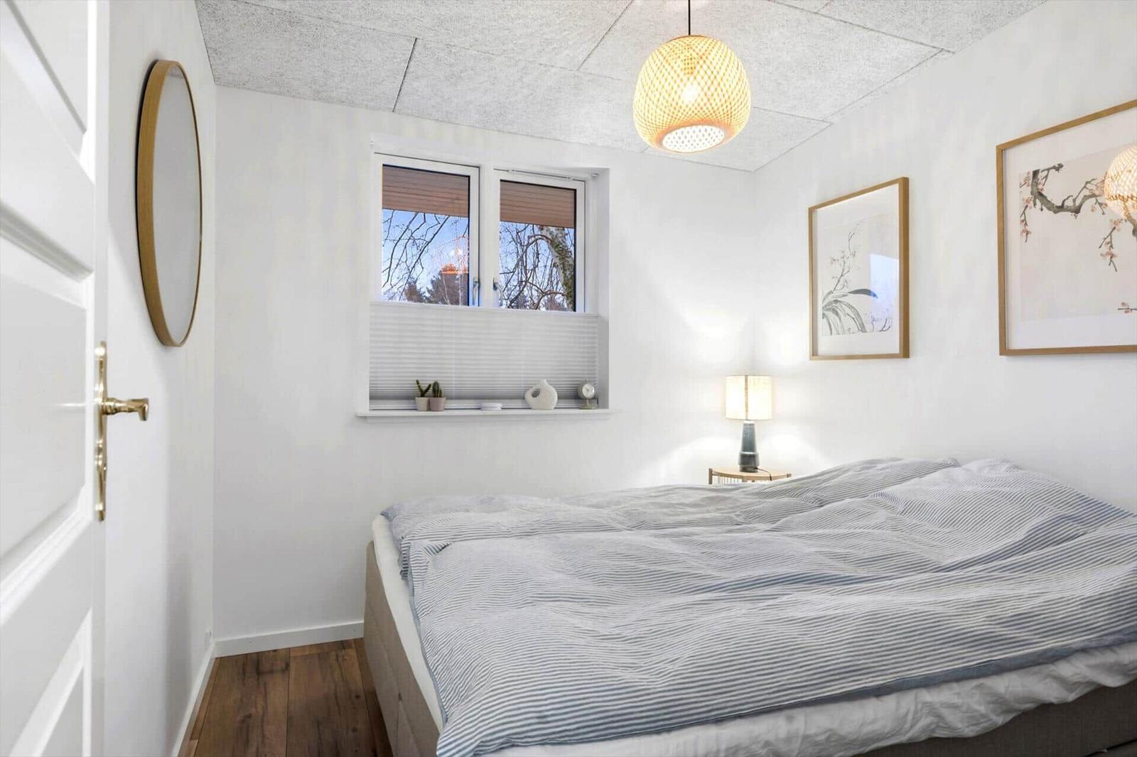Bedroom with bed, window, and quilt. Wooden floor and lamp.
