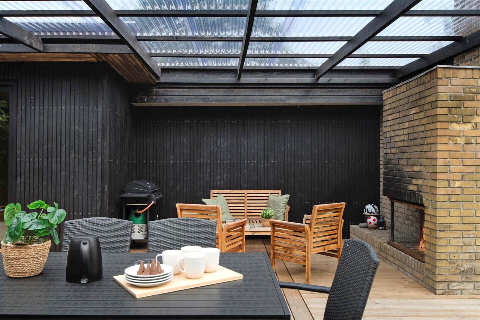 Outdoor area with grill, seating group, and fireplace under glass roof.