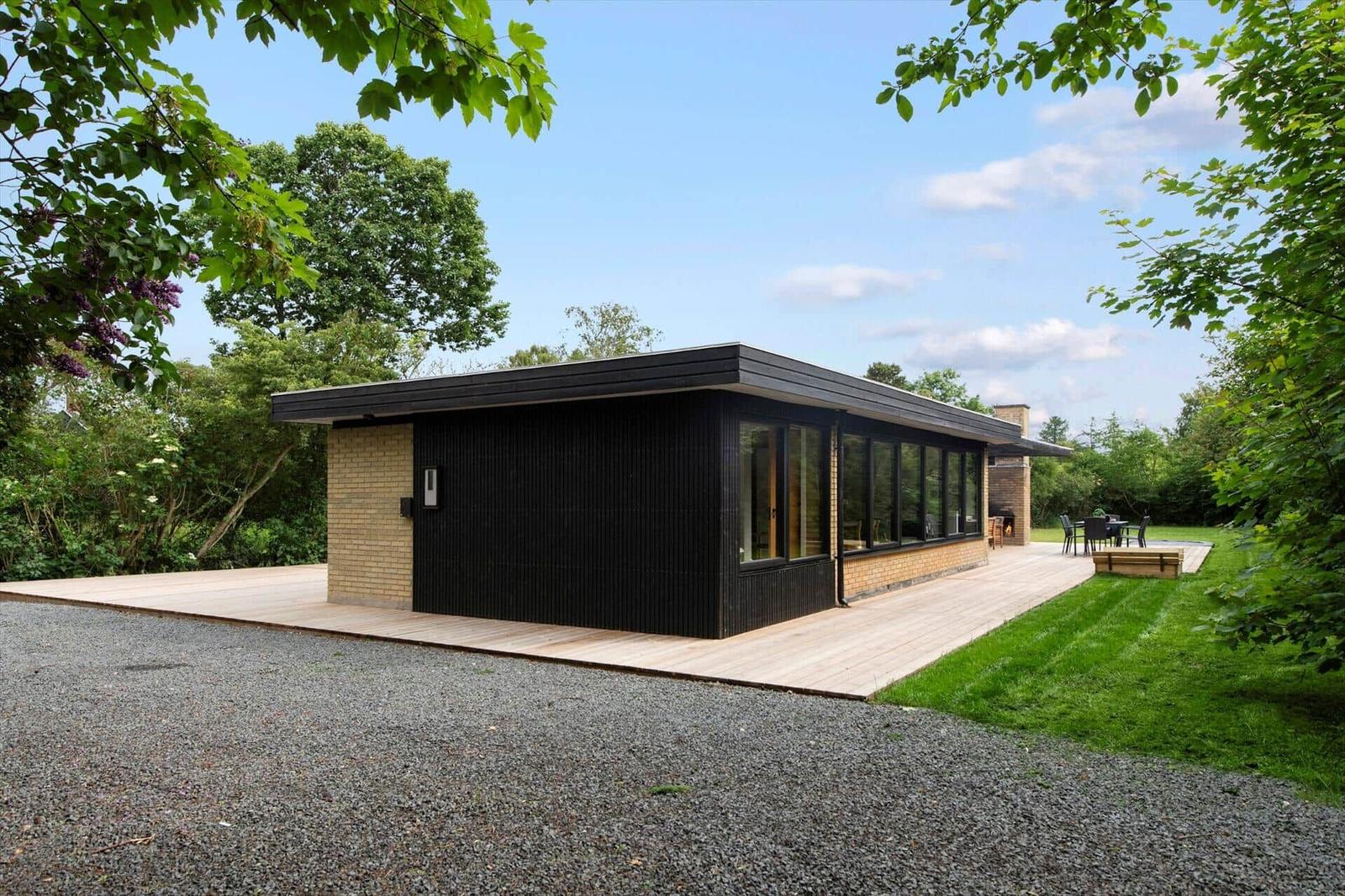 Modern villa with wooden terrace and garden. Black facade, large windows.