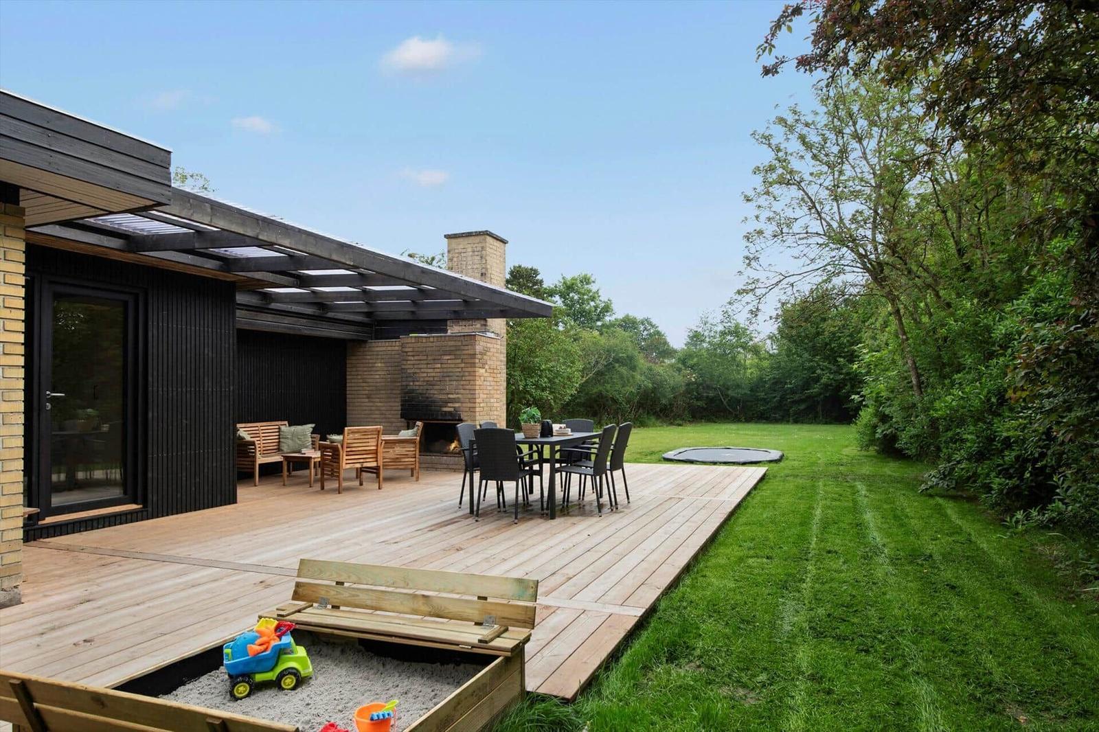 Wooden terrace with seating, grill, table and trampoline in the garden.