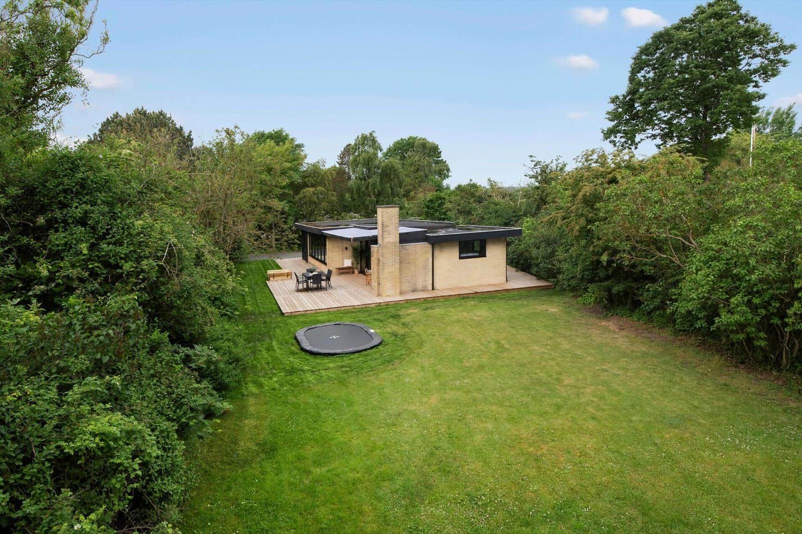 Modern villa with terrace, trampoline, and surrounding trees.